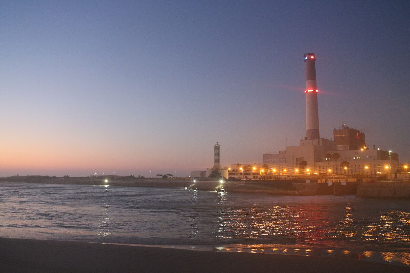 A power station on the coast with its lights on at dusk